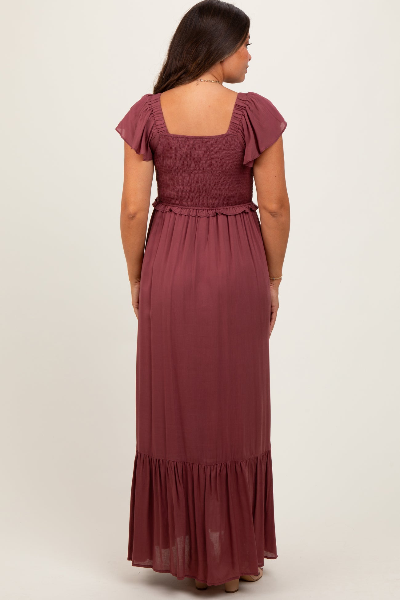 woman wearing a burgundy maternity maxi dress with a smocked bodice and flutter sleeves, viewed from the back