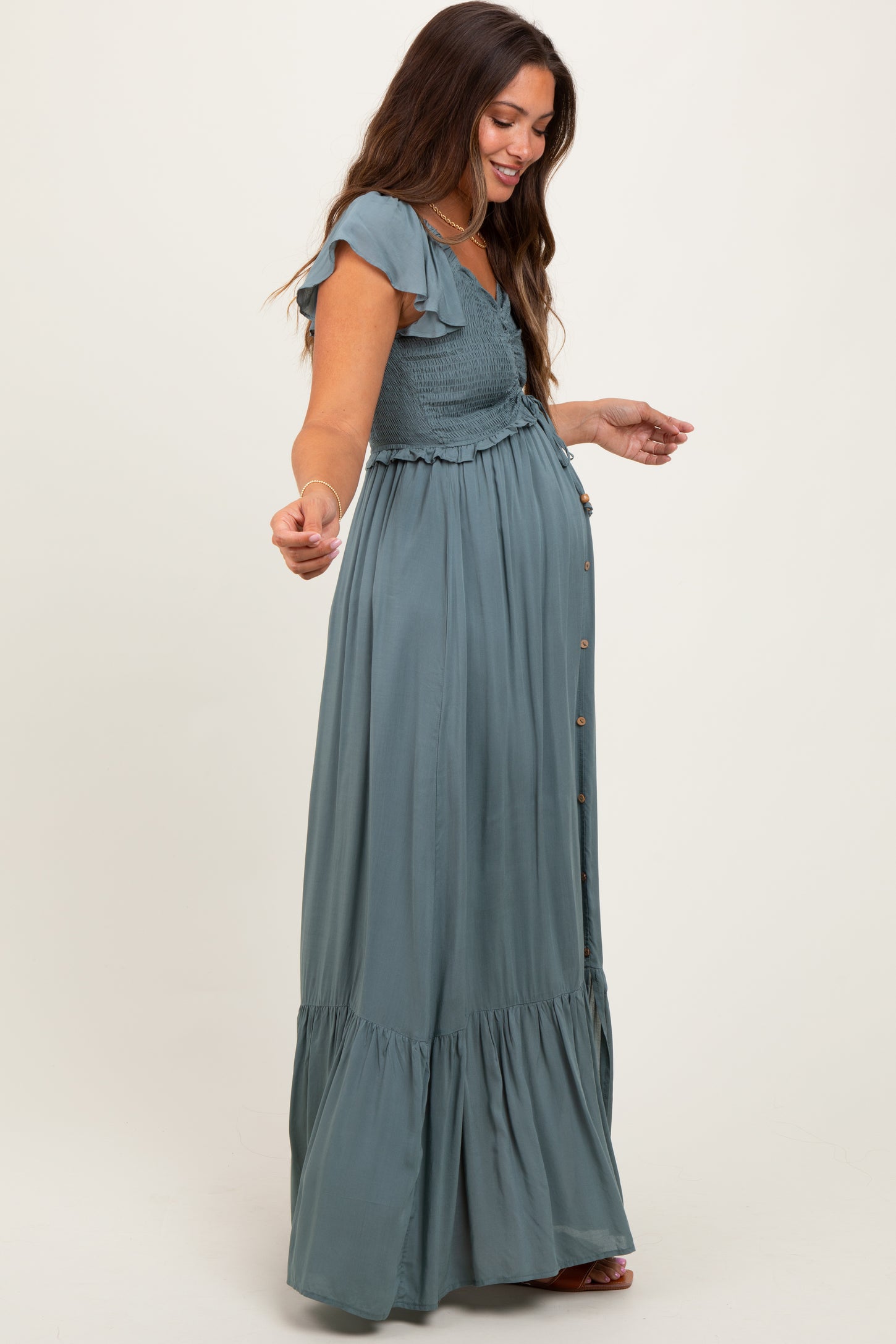 woman wearing a green maternity maxi dress with ruffle sleeves and a smocked bodice, showing her baby bump