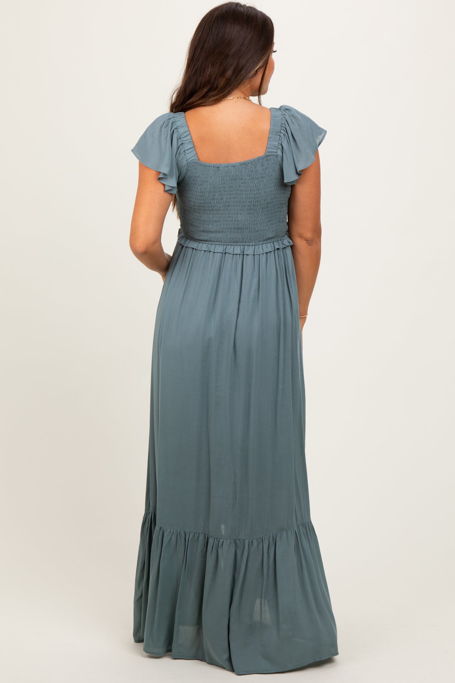 woman wearing a dusty blue maternity maxi dress with flutter sleeves and a smocked bodice, viewed from the back