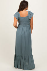 woman wearing a dusty blue maternity maxi dress with flutter sleeves and a smocked bodice, viewed from the back