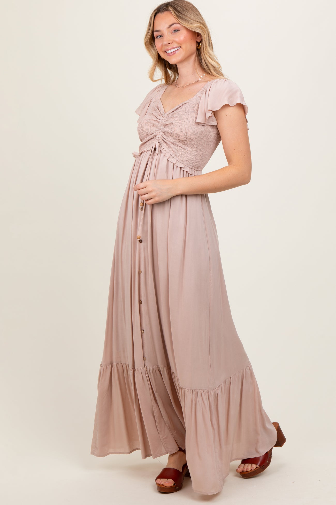 woman wearing a light pink maxi dress with a smocked bodice, flutter sleeves, and button details
