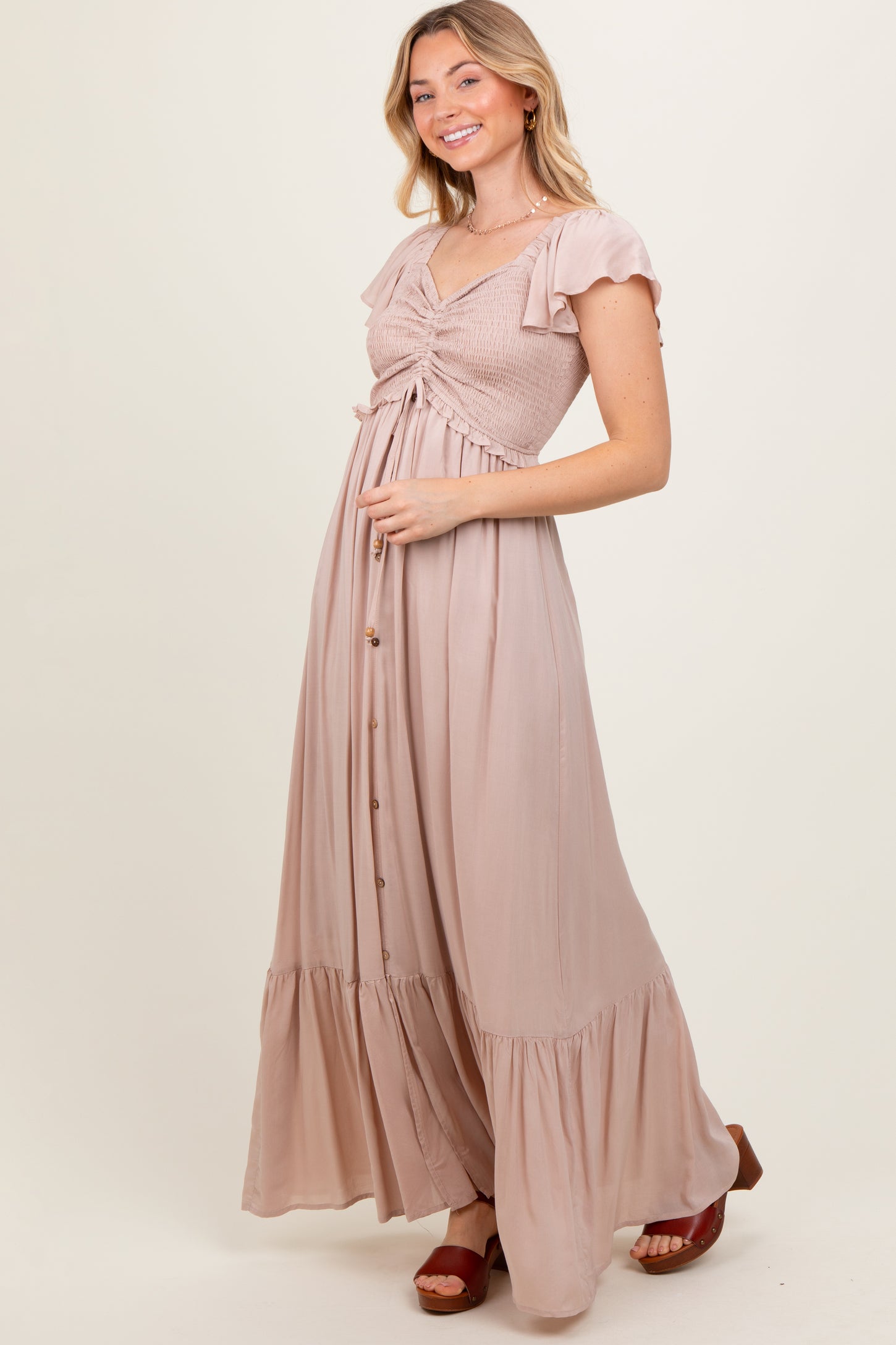 woman wearing a light pink maxi dress with a smocked bodice, flutter sleeves, and button details