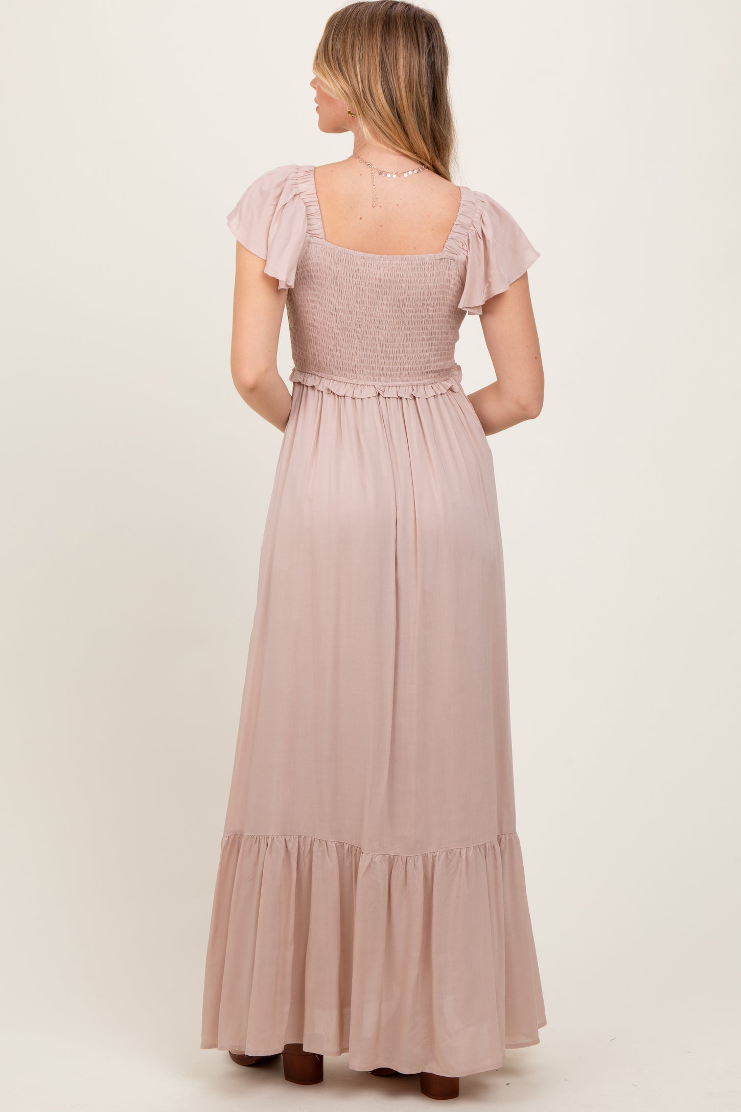woman wearing a dusty rose maxi dress with flutter sleeves and a smocked bodice, seen from the back