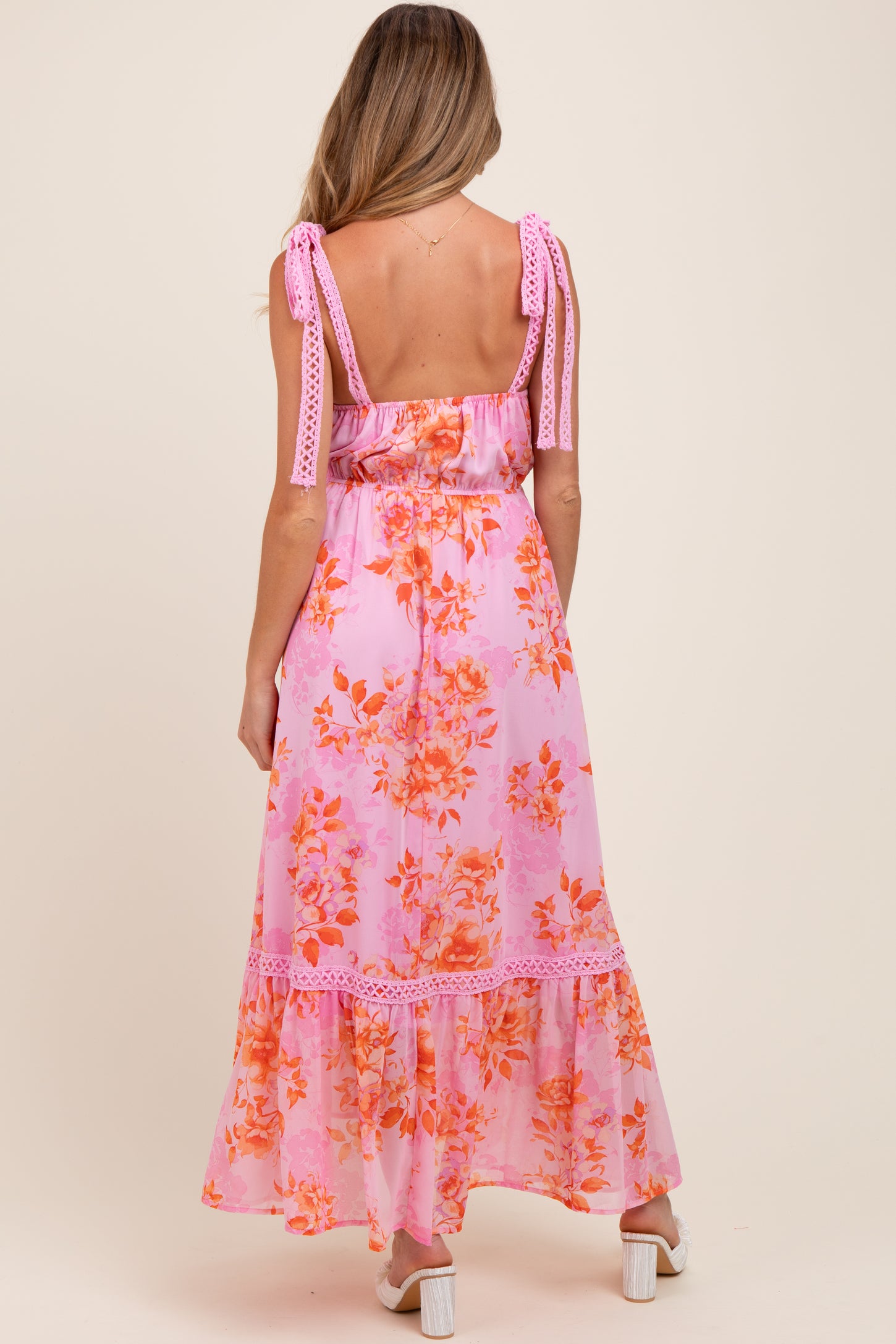 woman wearing a pink floral maternity maxi dress with adjustable tie straps and a tiered hem