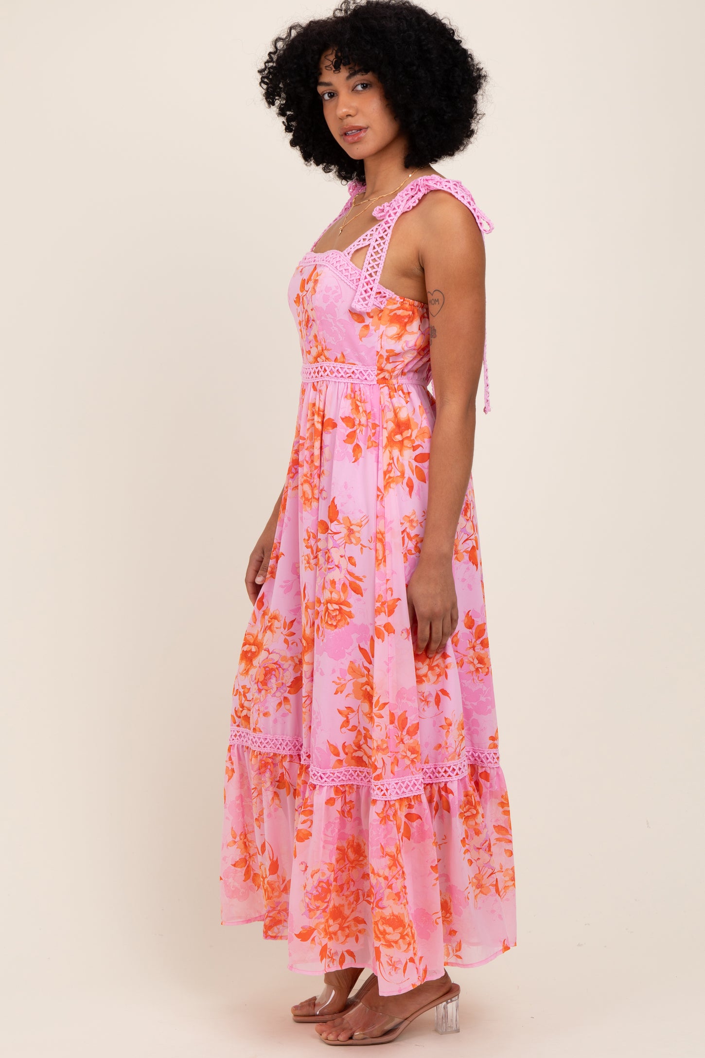 woman wearing a pink floral maxi dress with adjustable tie straps and lace trim details