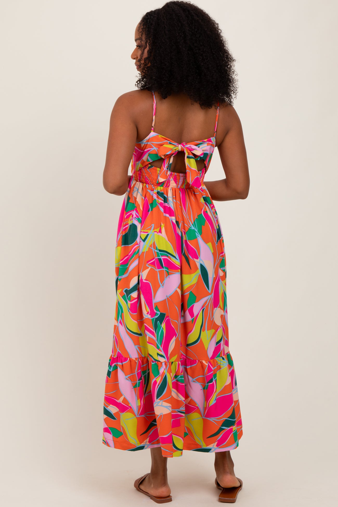woman wearing a pink and multicolor floral maxi dress with a tie back and adjustable straps
