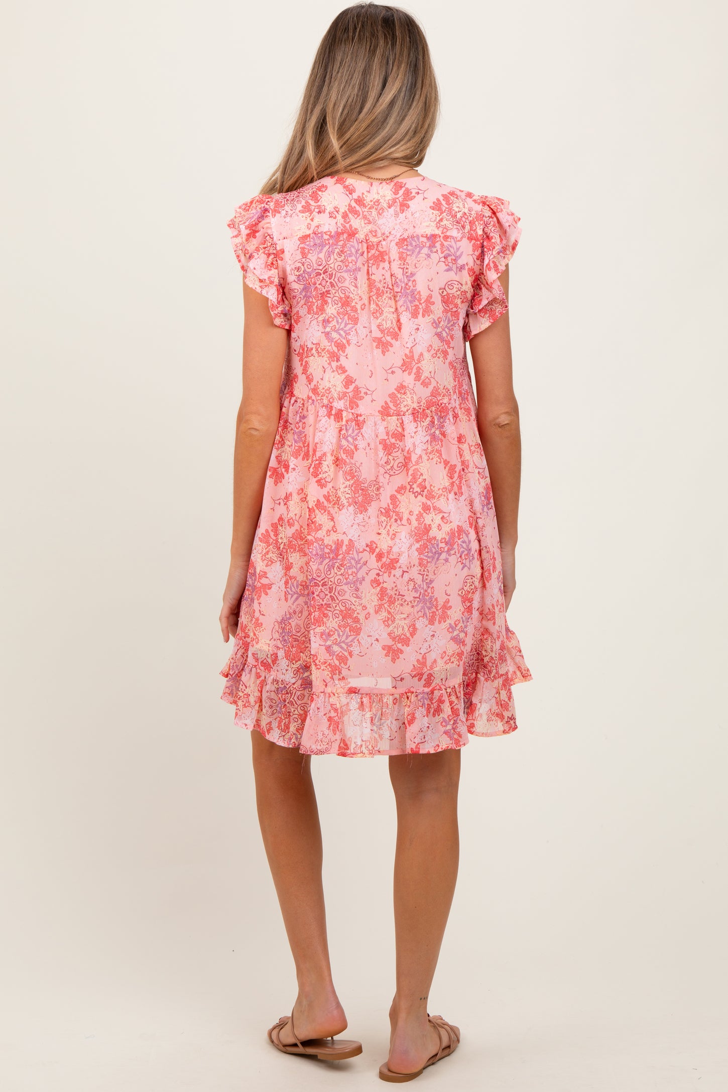 woman wearing a pink floral maternity dress with ruffled sleeves and a tiered hem, showing a baby bump from the back