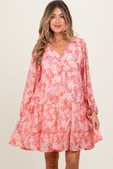 woman wearing a pink floral maternity dress with long sleeves and a tiered skirt, smiling at the camera