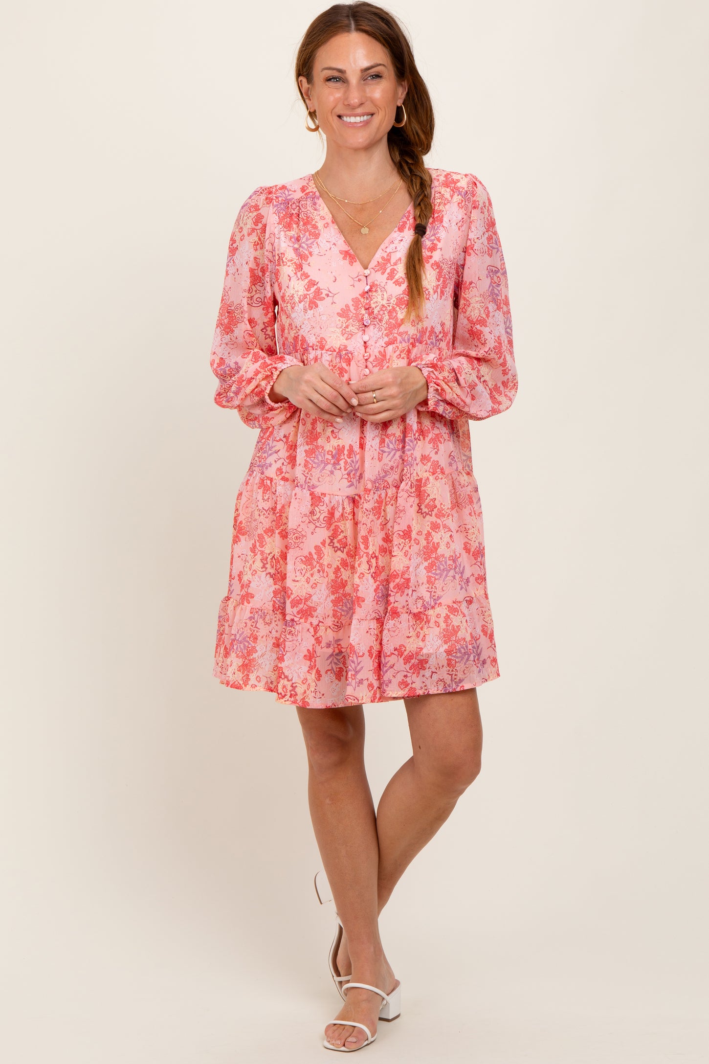 woman wearing a pink floral dress with a v-neck and long sleeves, standing with a smile