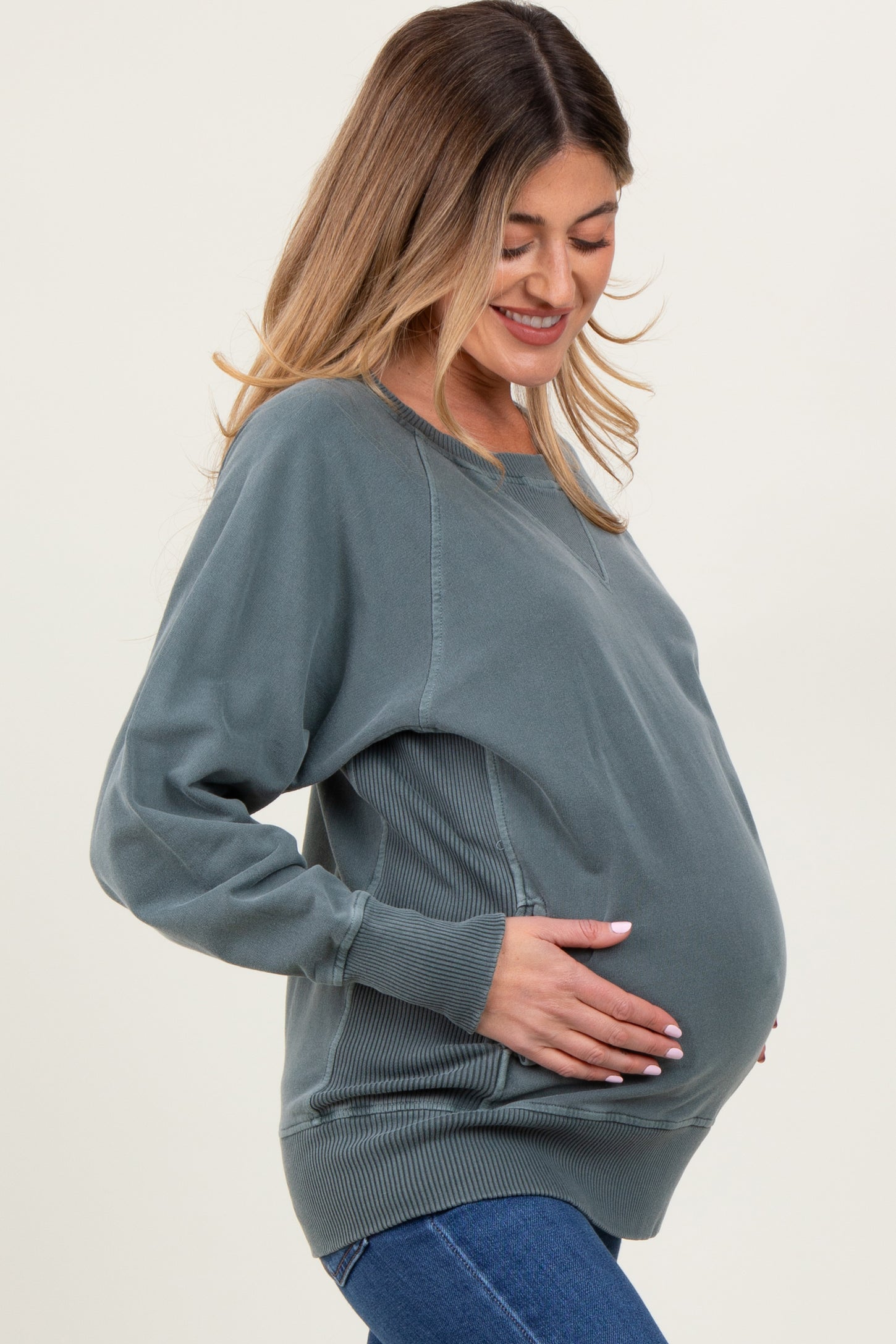 woman wearing a dusty green maternity sweatshirt and holding her baby bump