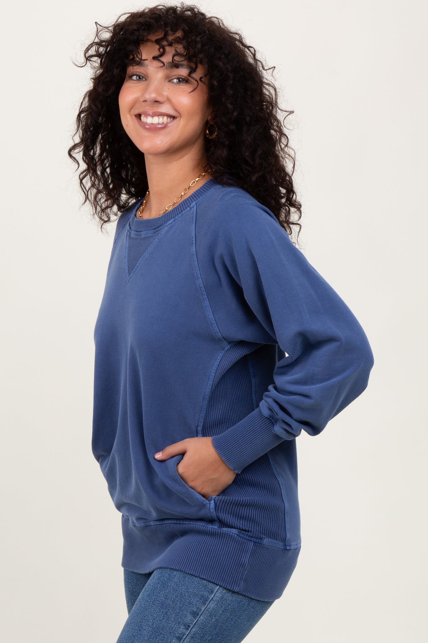 woman wearing a blue oversized sweatshirt with side pockets and a relaxed fit, smiling at the camera