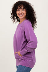 woman wearing a purple oversized sweatshirt with side pockets and ribbed details, smiling at the camera