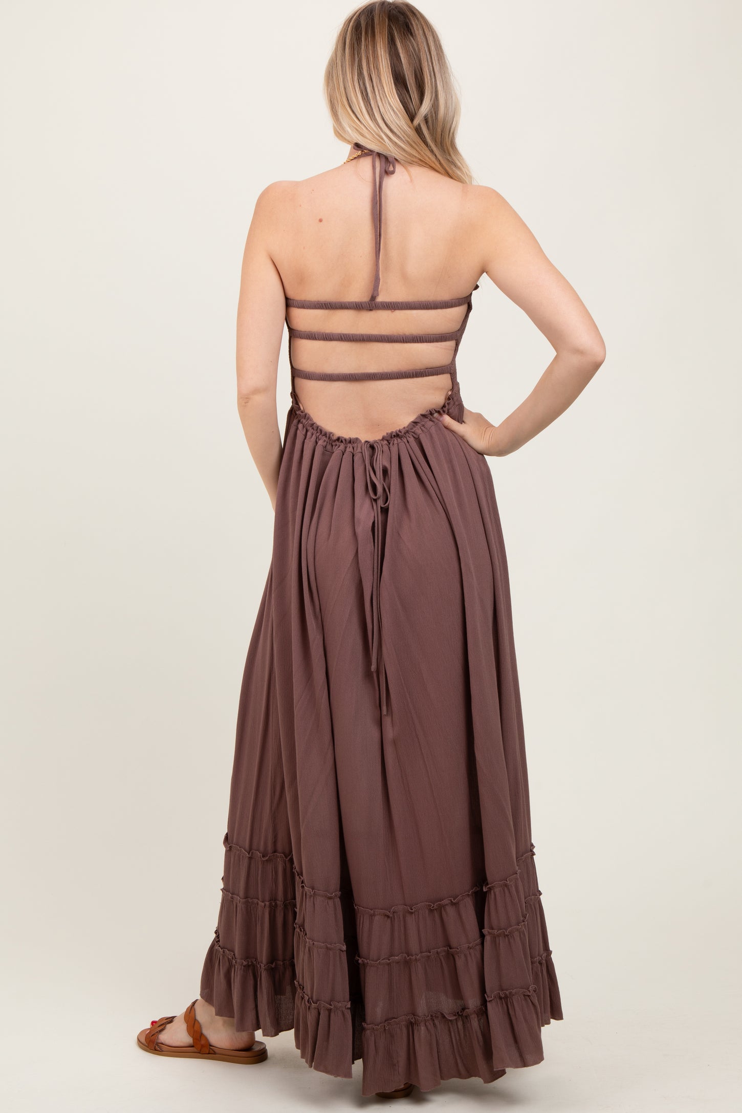 woman wearing a dusty mauve maxi dress with a halter neck and ruffled hem, showcasing an open back design