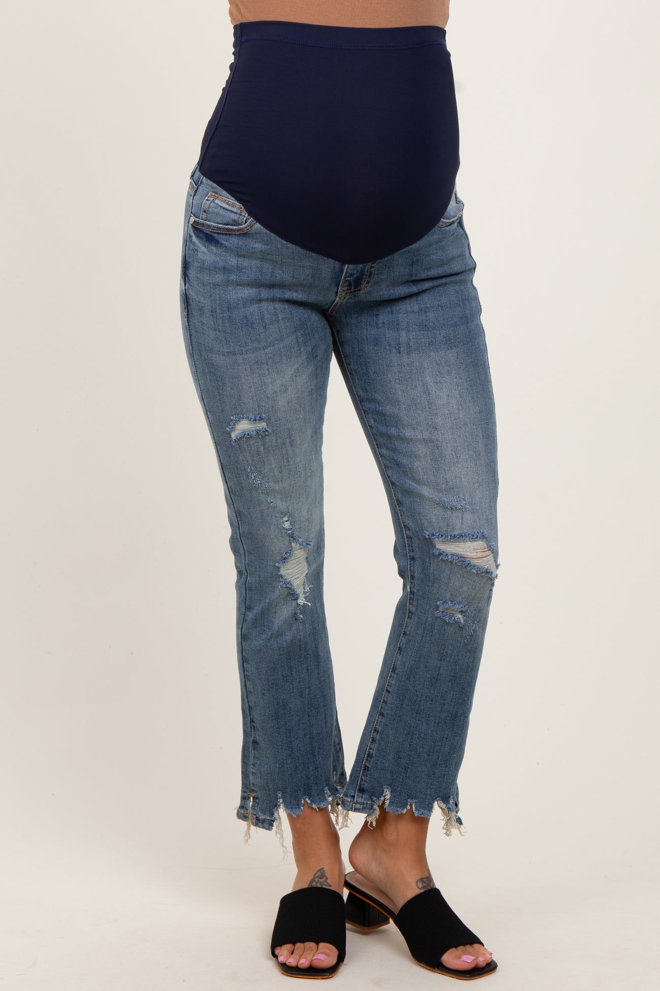 woman wearing blue distressed maternity jeans with a navy belly panel and frayed hem, showing her baby bump