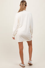 woman wearing a cream long sleeve maternity sweatshirt dress seen from the back with white sneakers