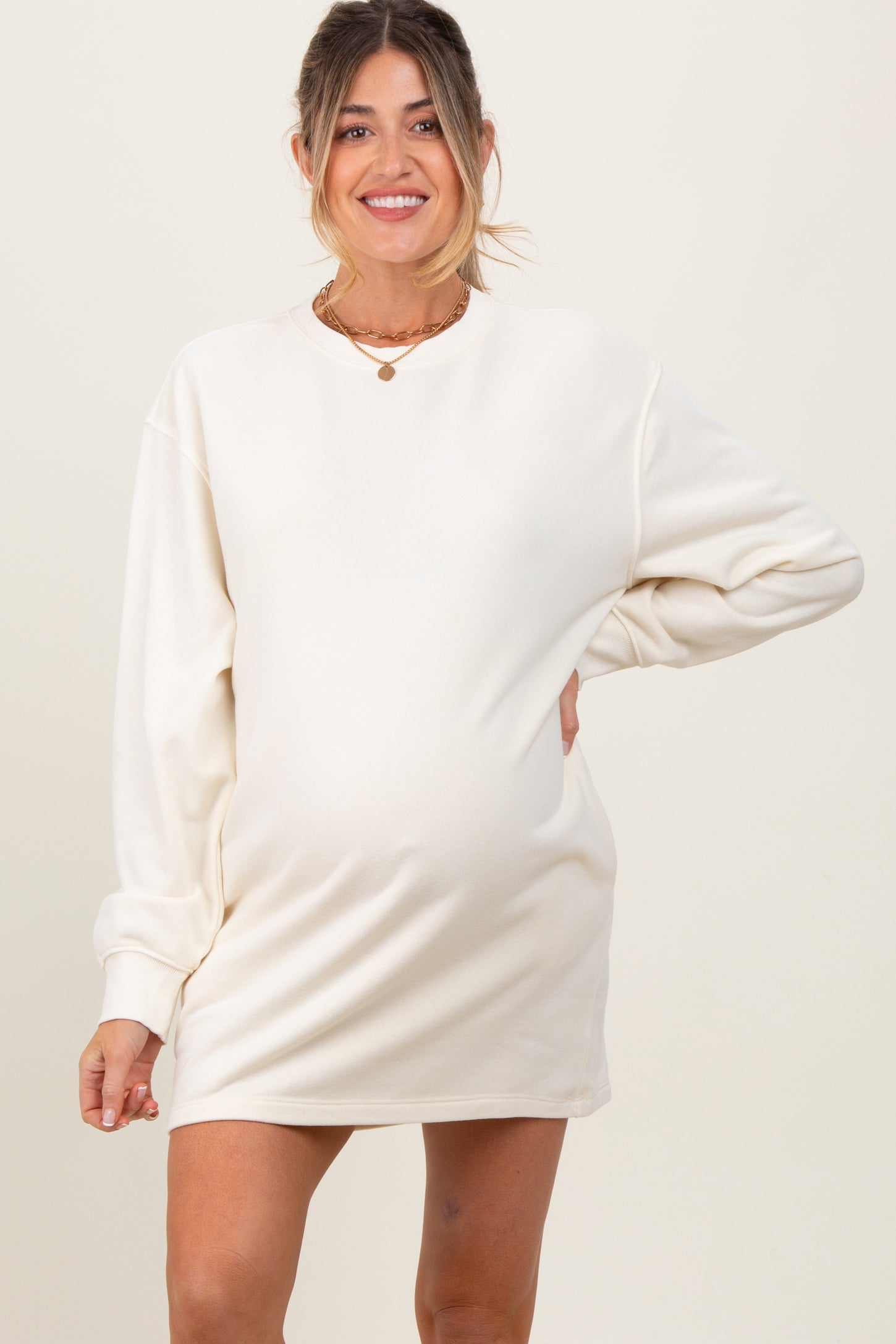 woman wearing a cream long sleeve maternity dress with a visible baby bump and smiling at the camera