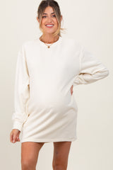 woman wearing a cream long sleeve maternity dress with a visible baby bump and smiling at the camera