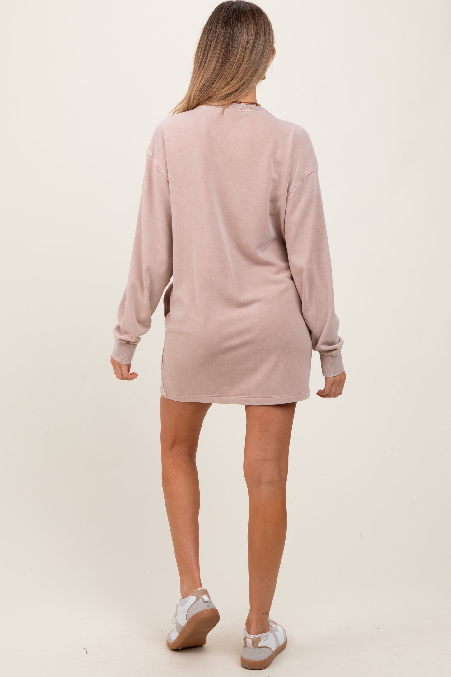 woman wearing a light pink maternity dress with long sleeves, standing with her back to the camera