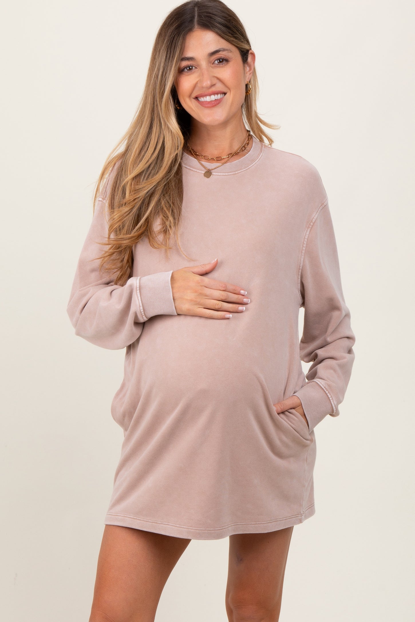 woman wearing a blush pink maternity sweatshirt dress and holding her baby bump
