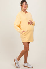 woman wearing a yellow maternity sweatshirt dress with pockets and a visible baby bump