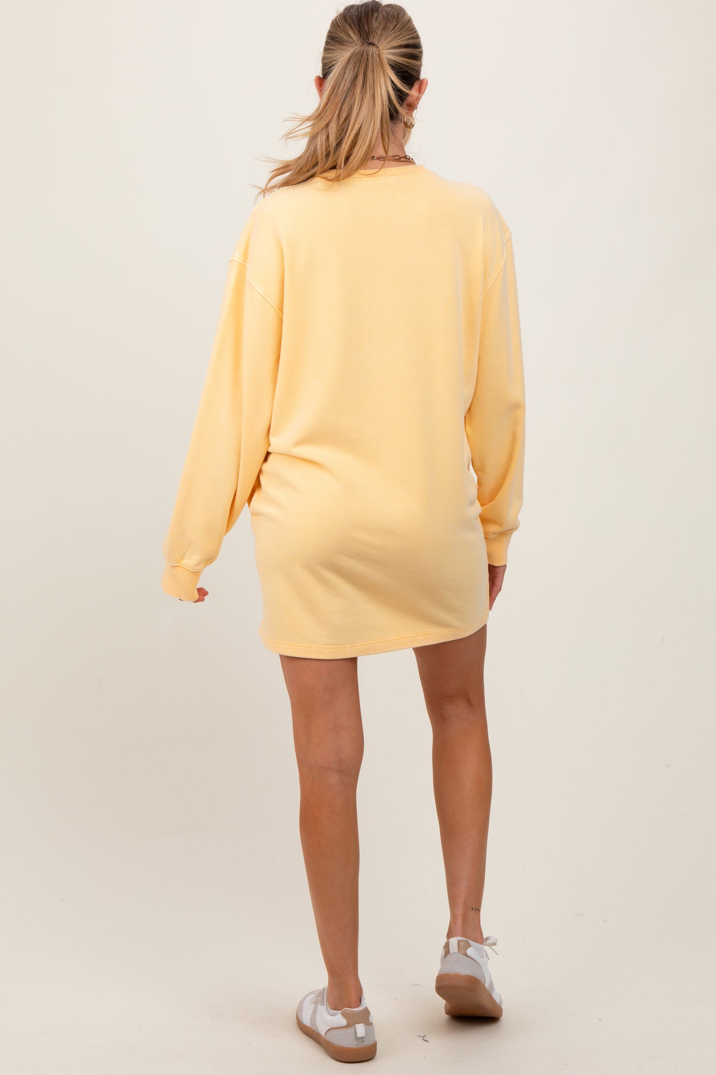 woman wearing a yellow oversized maternity sweatshirt dress, seen from the back, casual style with long sleeves