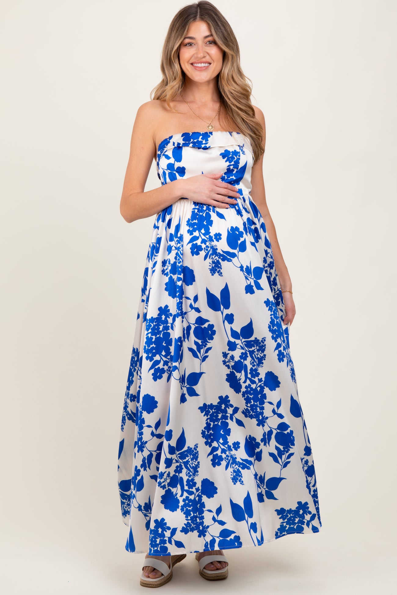 woman wearing a strapless floral patterned maternity maxi dress and holding her baby bump