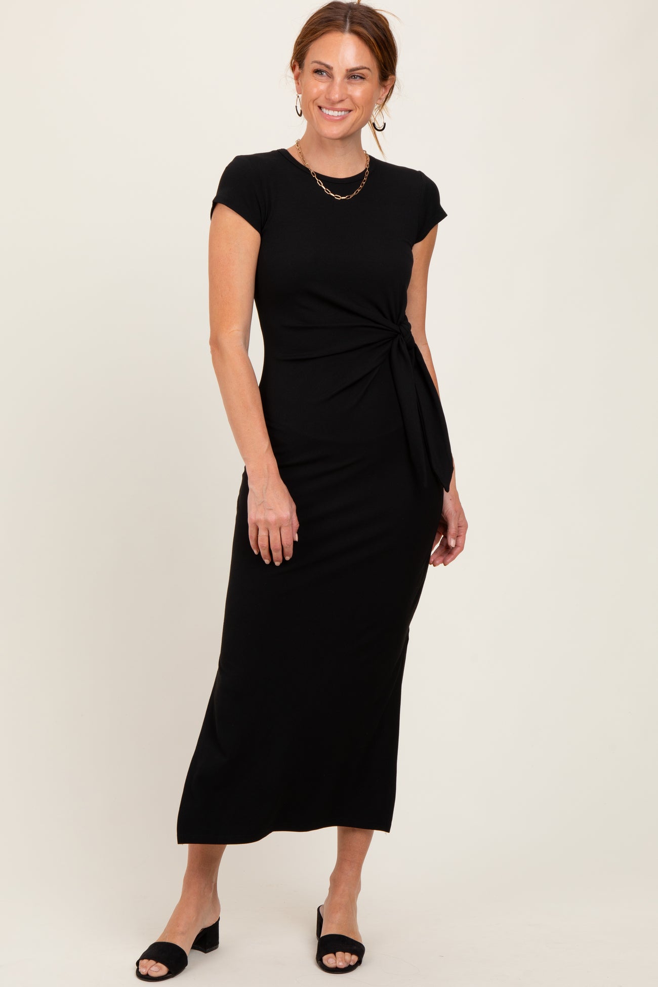 woman wearing a black cap sleeve maxi dress with a knot detail at the waist and styled with black heeled sandals