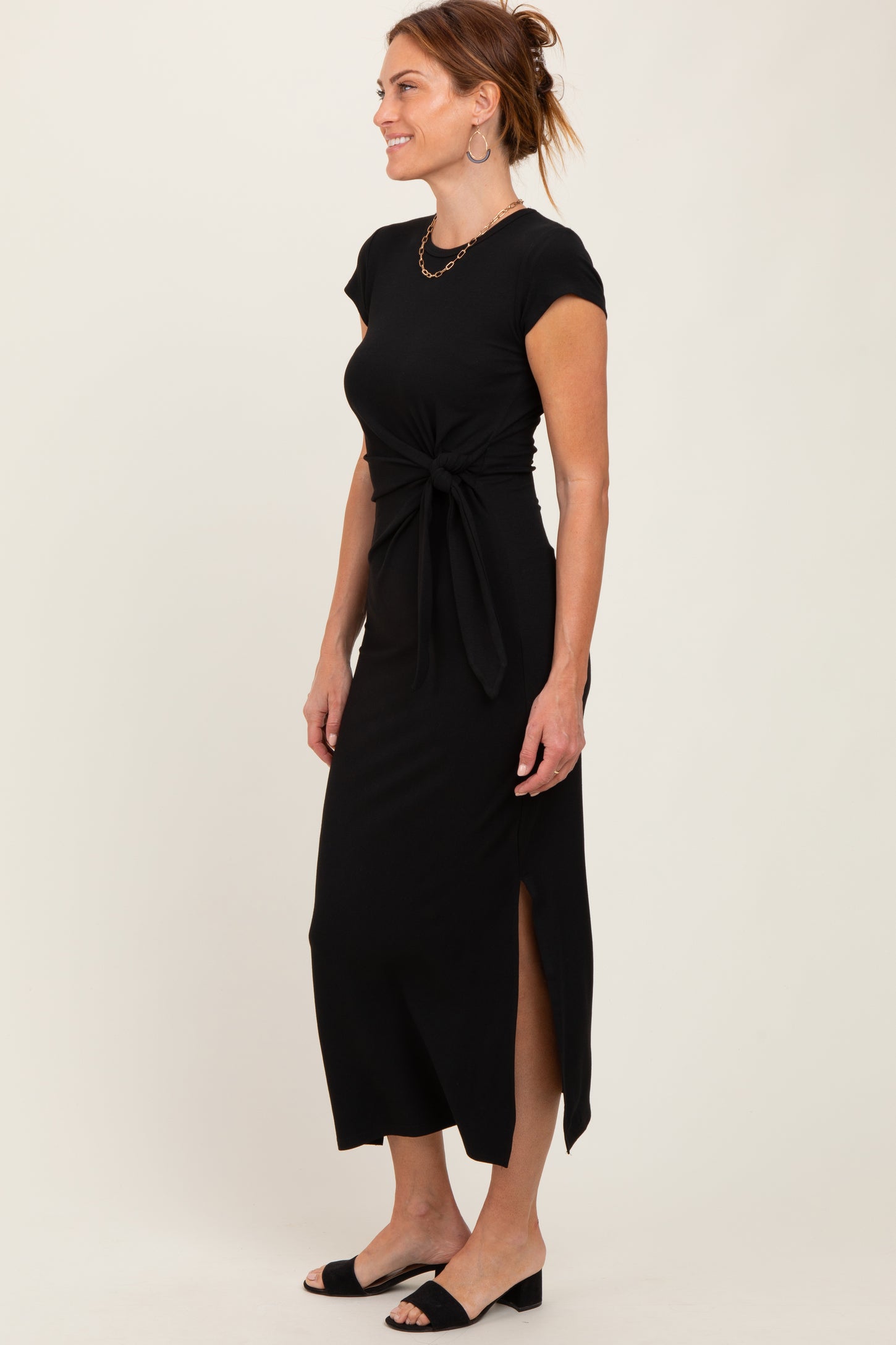 woman wearing a black cap sleeve maxi dress with a tie waist and side slits, styled with black slide-on shoes