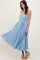 woman wearing a light blue pleated maxi dress with a tied waist detail and silver strappy sandals