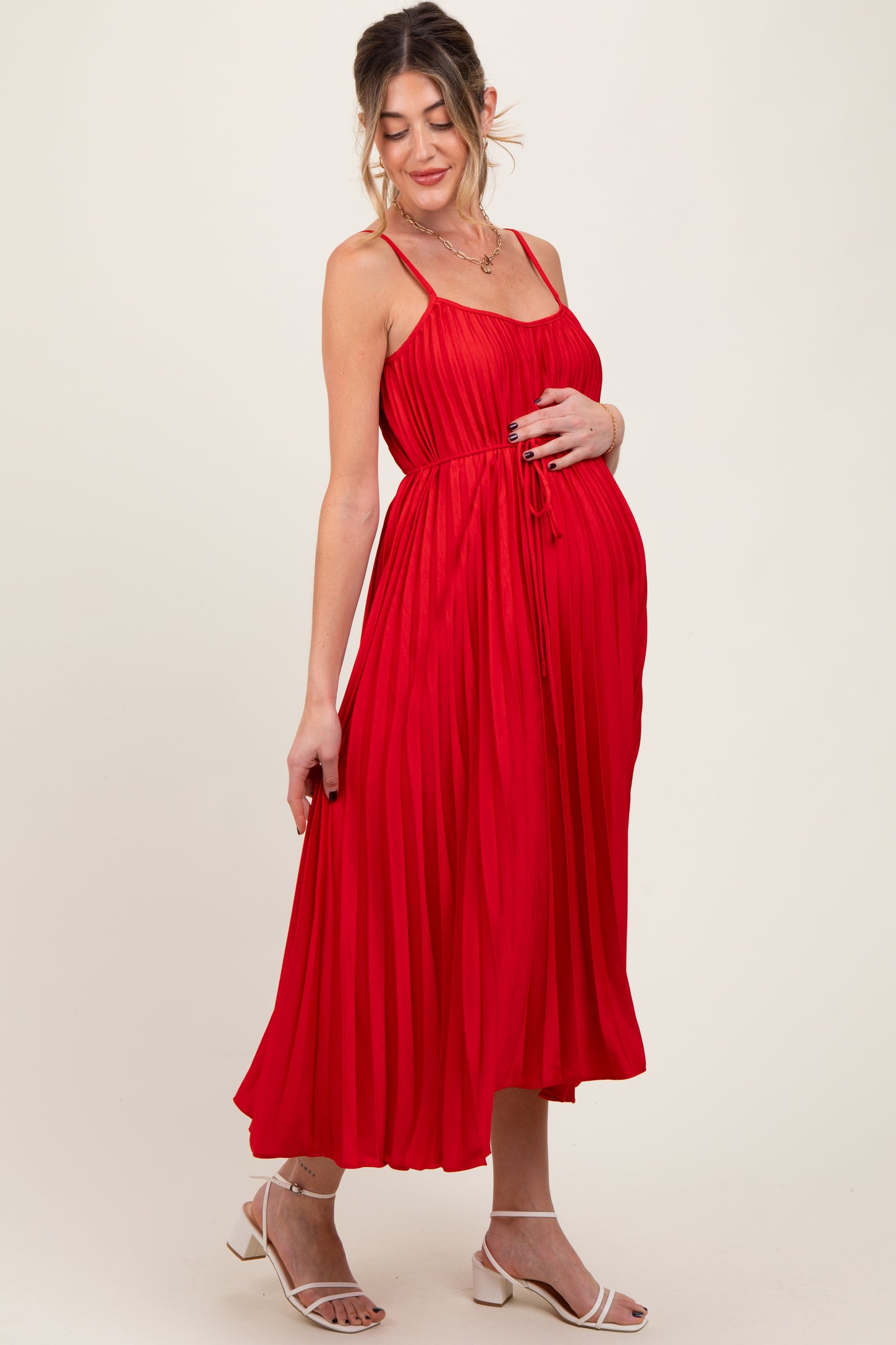woman wearing a red pleated maternity dress and holding her baby bump