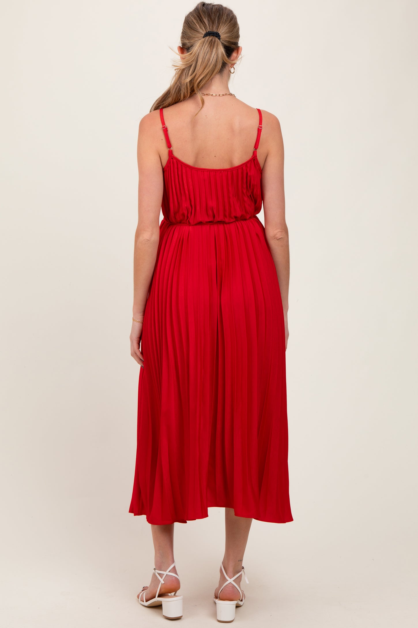 woman wearing a red pleated maternity dress with adjustable straps, showing the back view and a flowing silhouette
