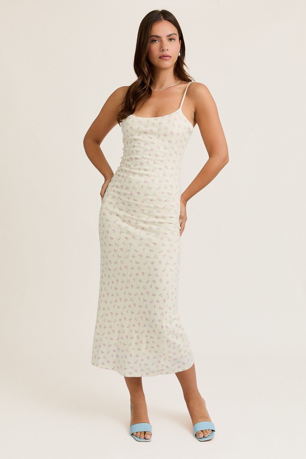 woman wearing a light floral midi dress with spaghetti straps and a fitted silhouette, posing confidently