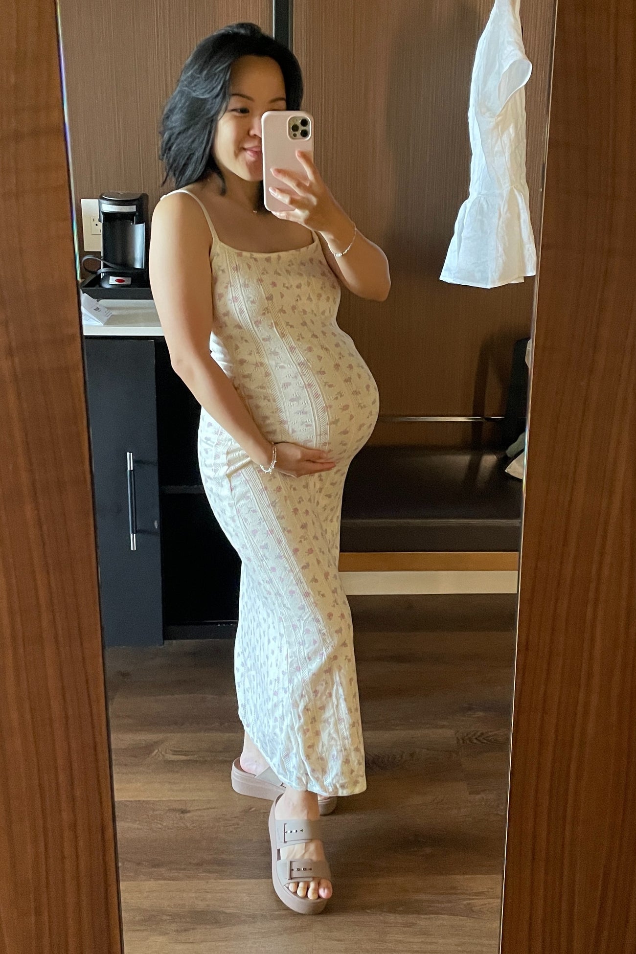 woman wearing a cream floral maternity maxi dress and holding her baby bump in front of a mirror