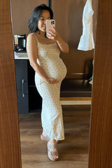 woman wearing a cream floral maternity maxi dress and holding her baby bump in front of a mirror