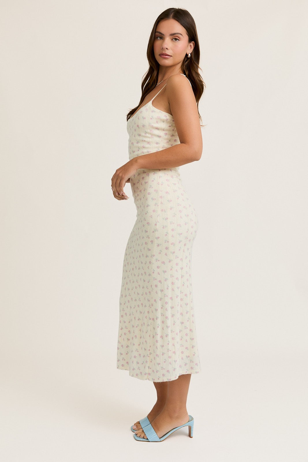 woman wearing a cream floral midi dress with thin straps and a fitted silhouette, styled with blue heeled sandals
