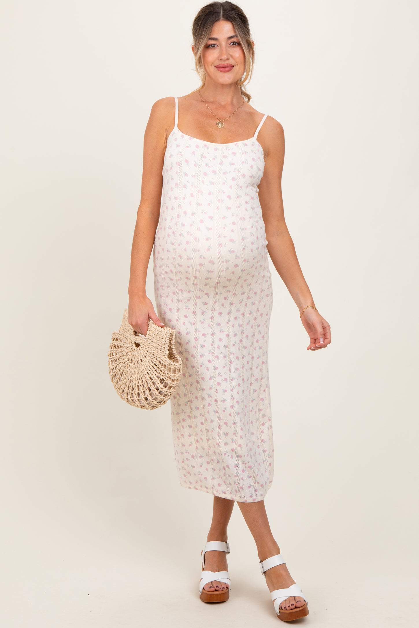 woman wearing a white floral print maternity dress with spaghetti straps and a visible baby bump