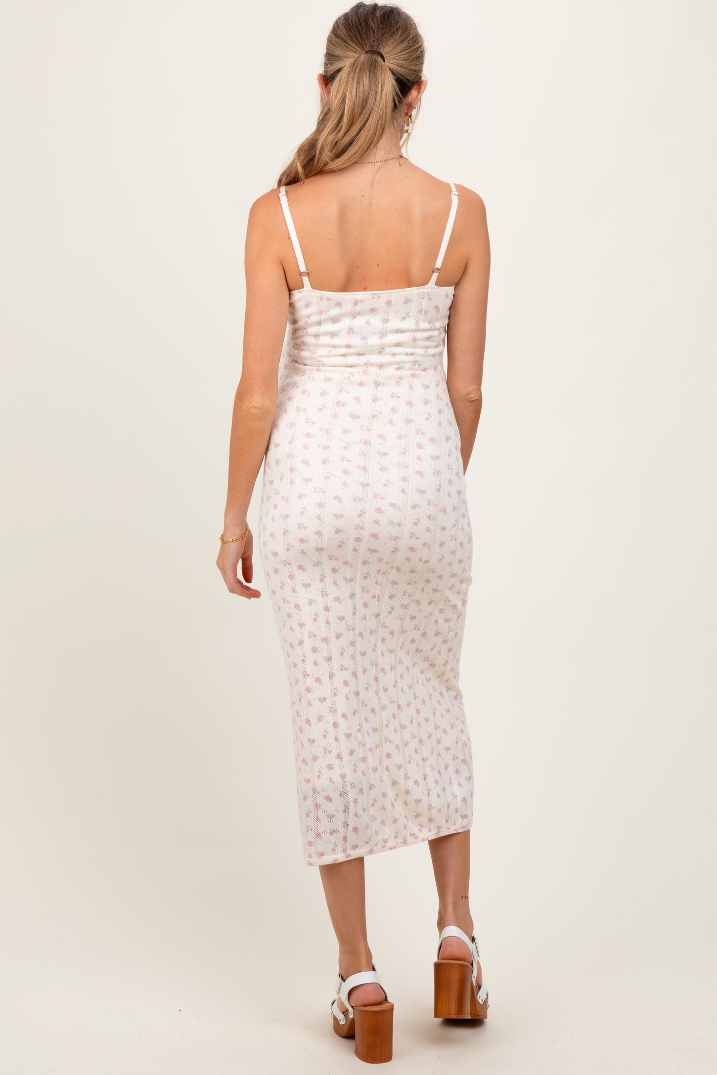woman wearing a floral print maternity dress with thin straps, showing a fitted silhouette and mid-calf length