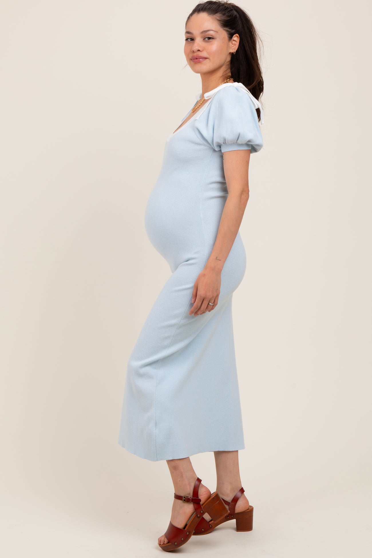 woman wearing a light blue maternity dress with puff sleeves, showing her baby bump, and paired with brown heeled sandals