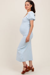 woman wearing a light blue maternity dress with puff sleeves, showing her baby bump, and paired with brown heeled sandals