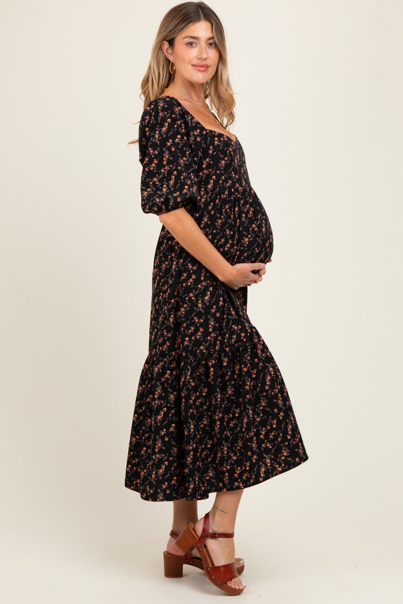 woman wearing a black floral maternity dress with a ruffled hem and holding her baby bump