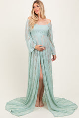 woman wearing a light green lace maternity gown with off-the-shoulder sleeves and a side slit, holding her baby bump