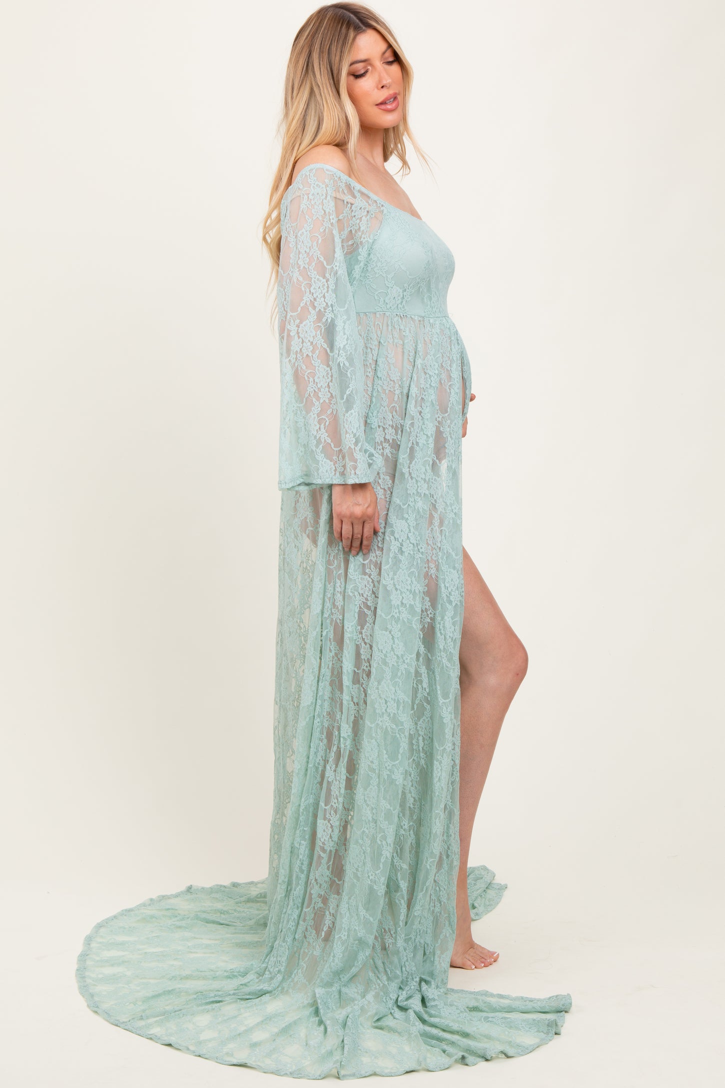 woman wearing a mint green lace maternity gown with long sleeves and a flowing train, showcasing her baby bump