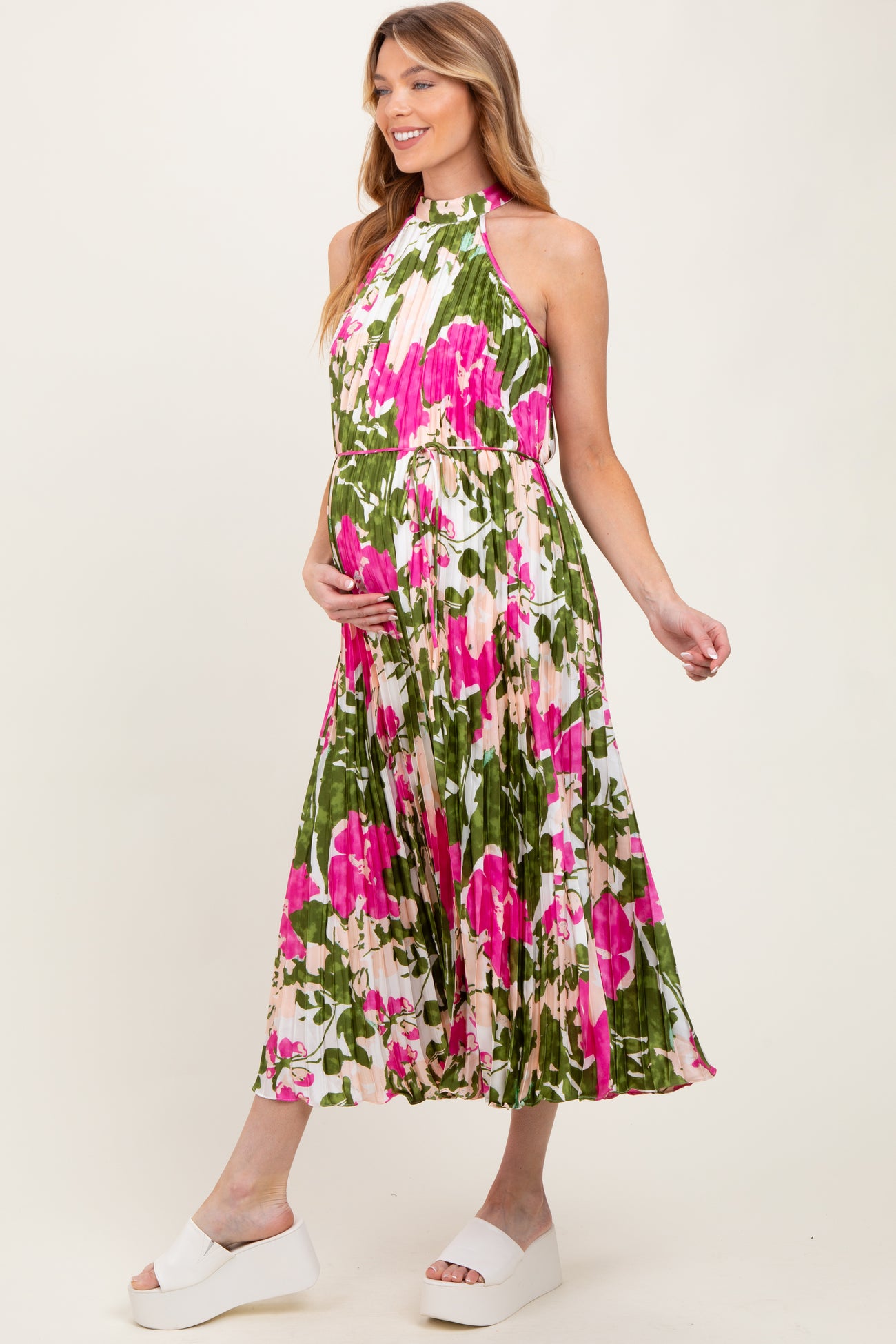 woman wearing a floral maternity dress with a high neck and flowing skirt, holding her baby bump
