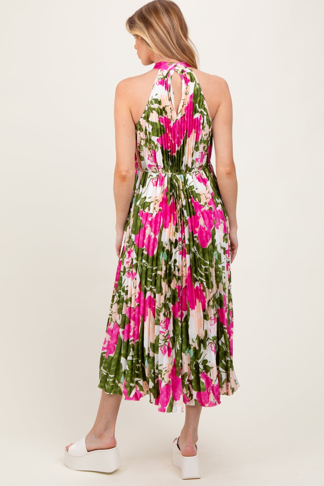 woman wearing a floral maternity dress with a halter neck and pleated skirt, featuring pink and green colors