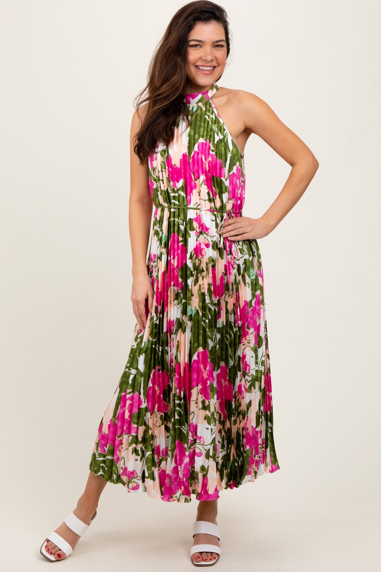 woman wearing a sleeveless floral maxi dress with pink and green hues, standing and smiling