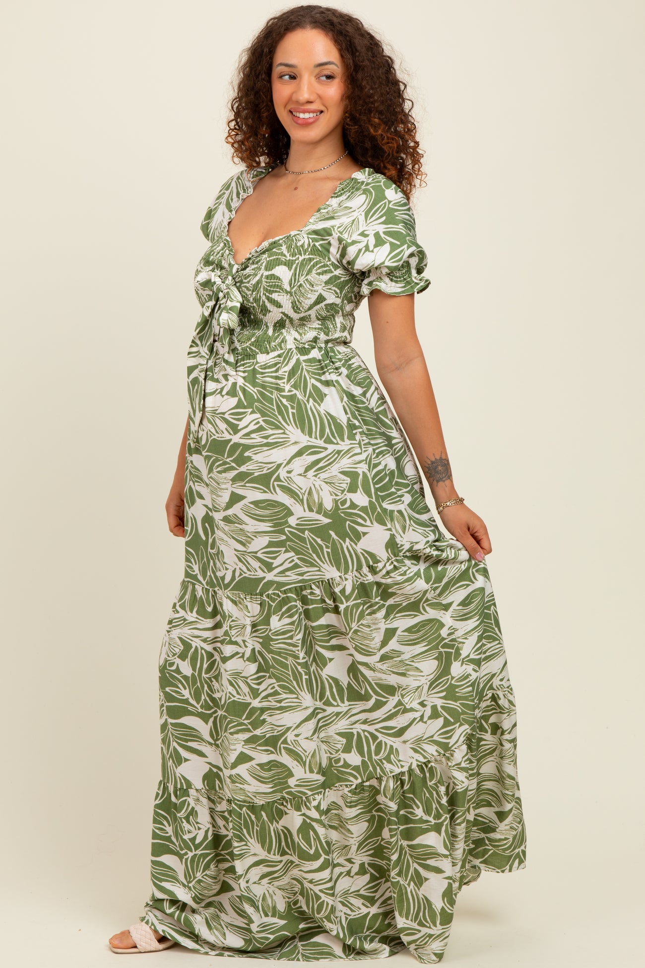 woman wearing a green floral print maternity maxi dress with short puff sleeves and a smocked bodice, showing her baby bump