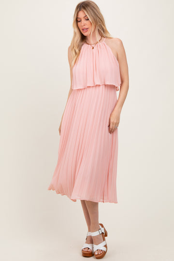 woman wearing a light pink pleated midi dress with a high neckline and layered bodice, styled with white sandals
