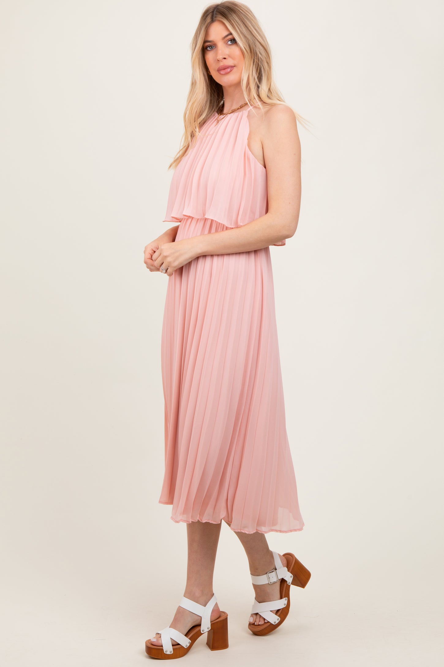 woman wearing a light pink pleated midi dress with a layered design and strappy heels