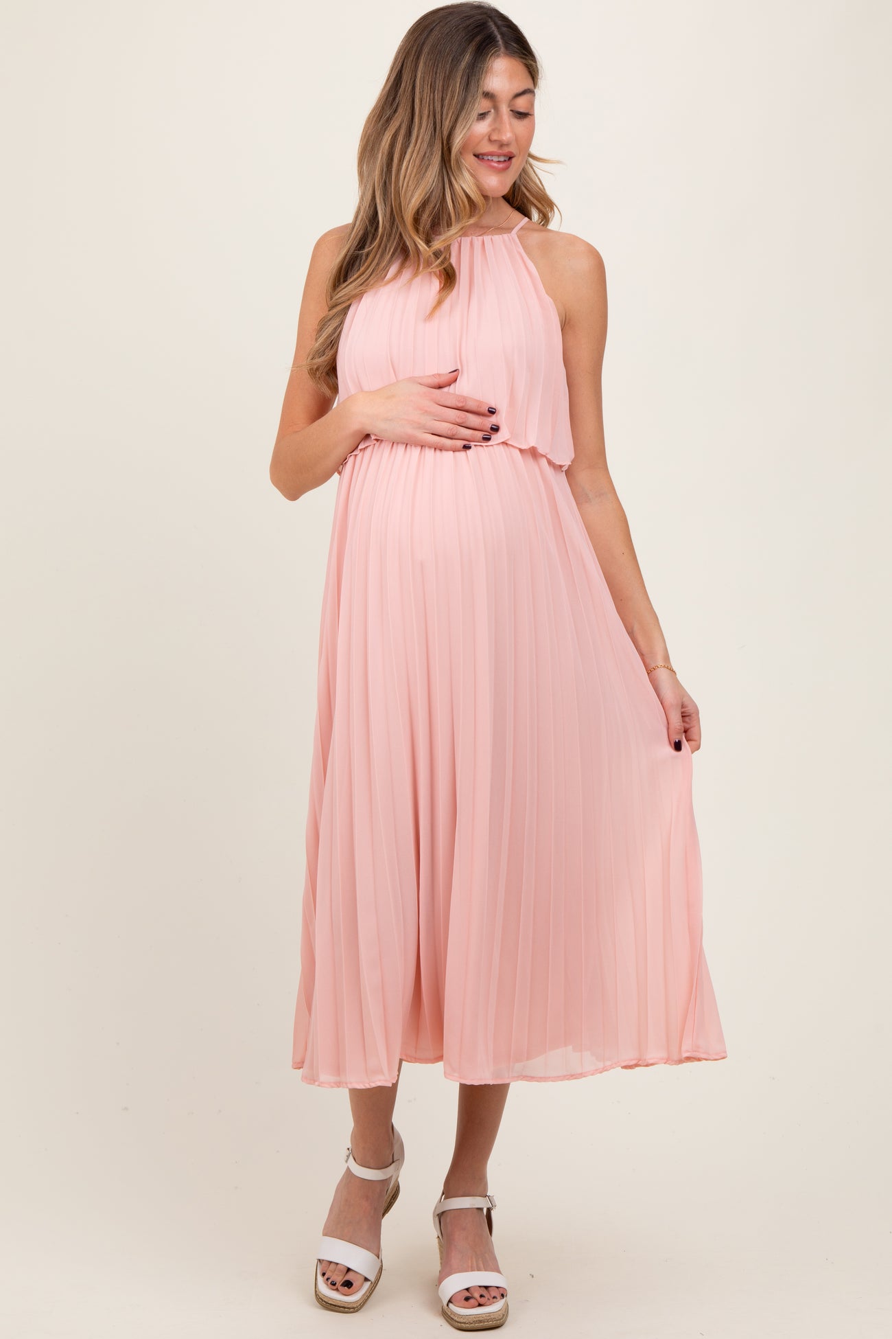 woman wearing a light pink pleated maternity dress and holding her baby bump
