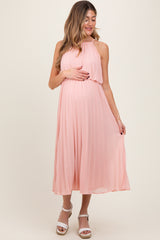woman wearing a light pink pleated maternity dress and holding her baby bump